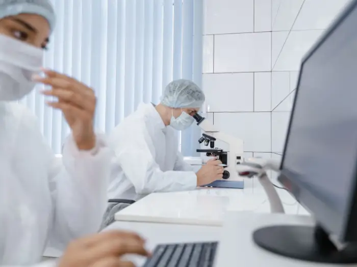 A technician examining a sample vial beside a laboratory screen