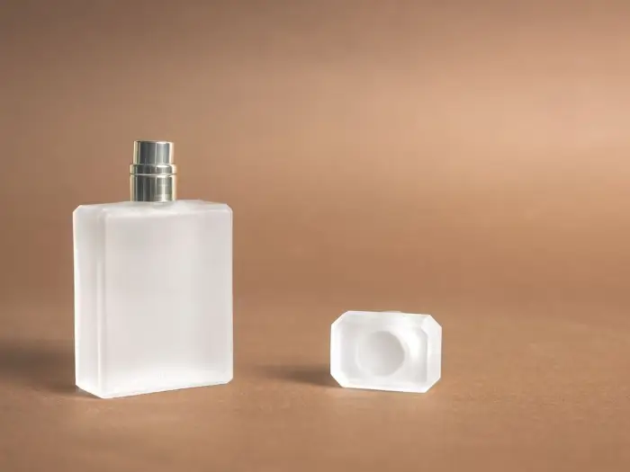 A frosted glass fragrance bottle on a warm neutral background
